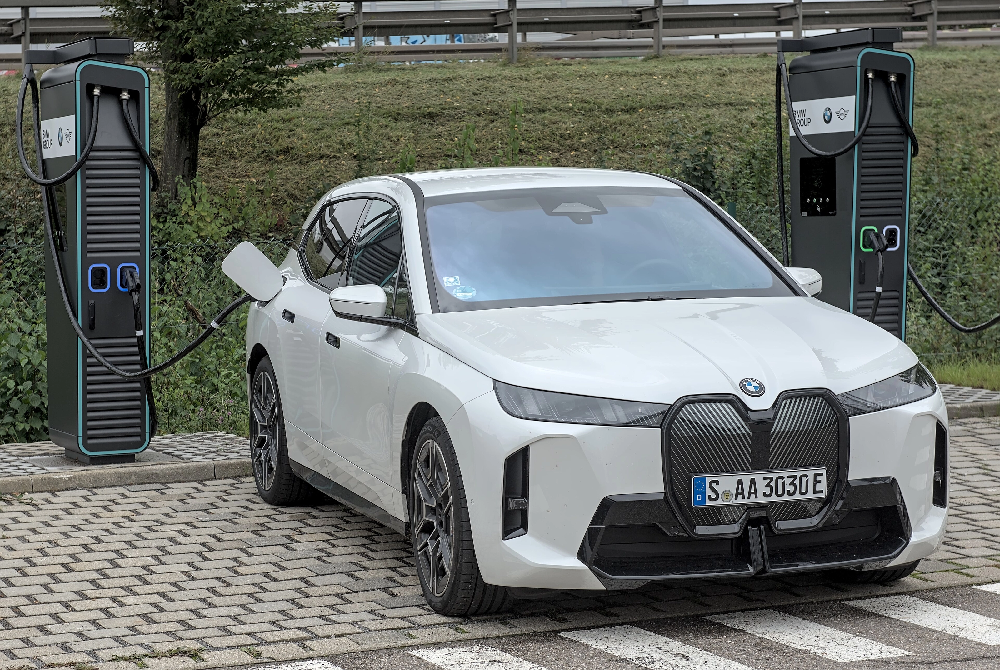 Weißer BMW iX mit dem Kennzeichen S-AA 3030E, per Kabel an eine Schnellladesäule angeschlossen