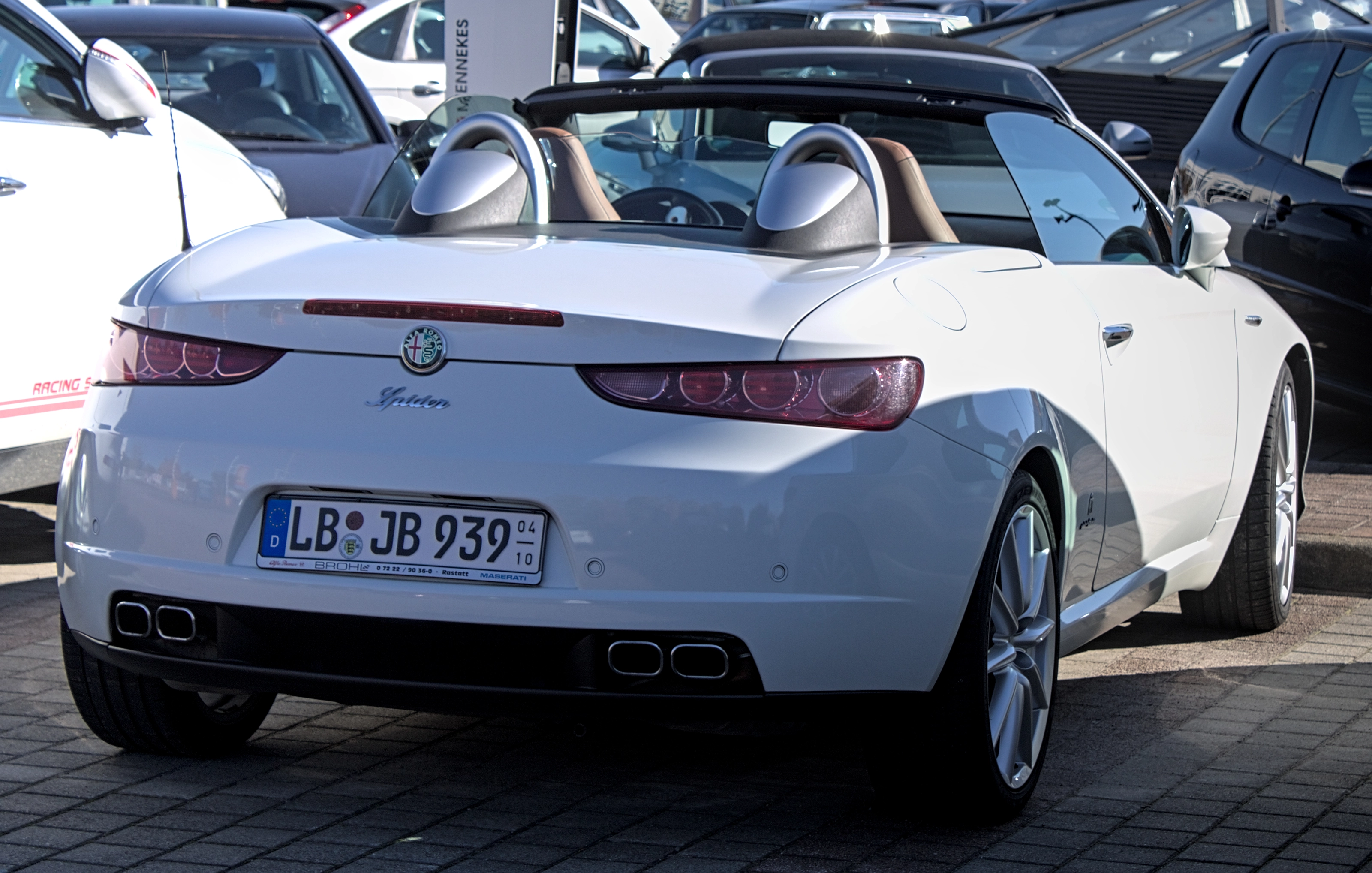 Weißer Alfa Romeo Spider von hinten auf einem Parkplatz, am Heck ein Saisonkennzeichen mit dem Zeitraum 04 bis 10
