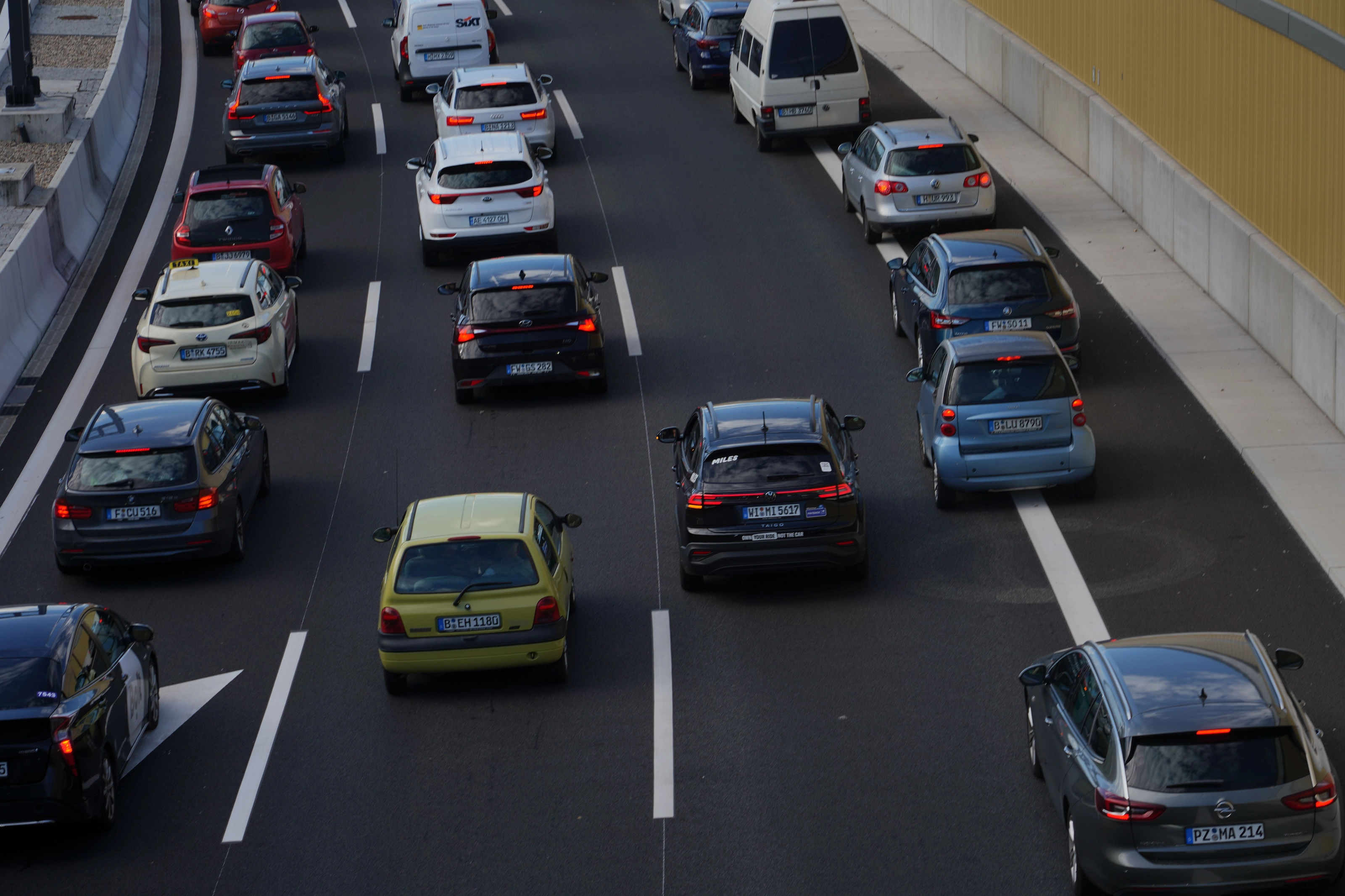 Blick von einer Brücke auf die Berliner Stadtautobahn A100: zahlreiche Autos von hinten in mehreren Spuren, ihre deutschen Kennzeichen mit Kombinationen wie B-LU 8790, WI-MI 5617 und PZ-MA 214 sind lesbar