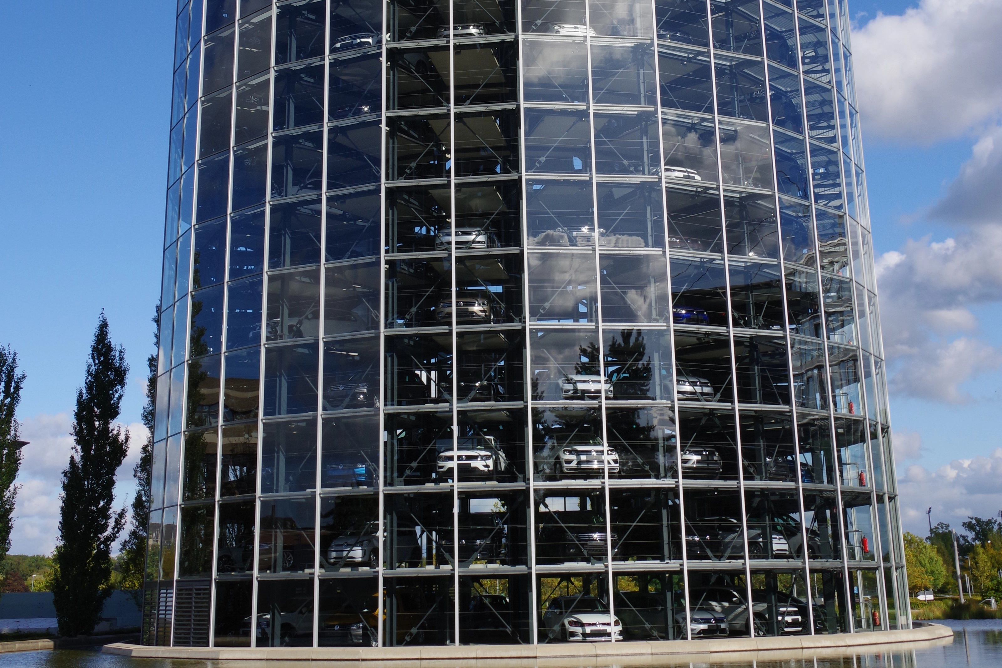 Gläserner Autoturm der Autostadt Wolfsburg unter blauem Himmel, hinter der Fassade stehen auf mehreren Etagen Neuwagen zur Auslieferung bereit